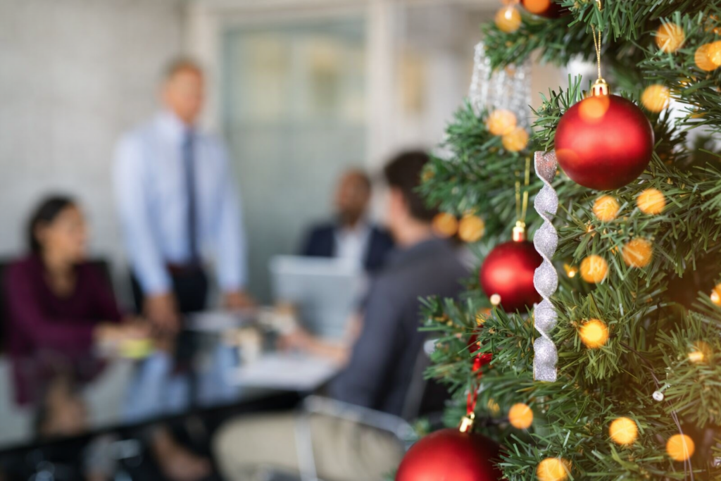 Vánočně vyzdobená kancelář s vánočním stromkem a kolegy v pozadí, symbol klidnějšího pracovního tempa na konci roku